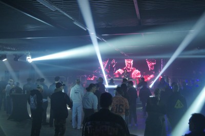 Un bus stationné de nuit devant un bâtiment illuminé, avec des passants en arrière-plan.