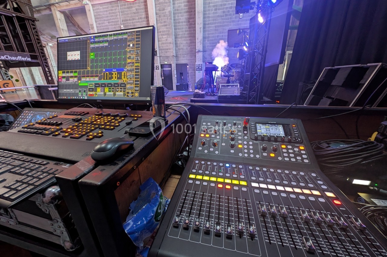 Poste de régie technique avec une console de mixage, un écran de contrôle et des équipements de scène en arrière-plan.
