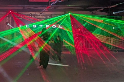 Un bus stationné de nuit devant un bâtiment illuminé, avec des passants en arrière-plan.