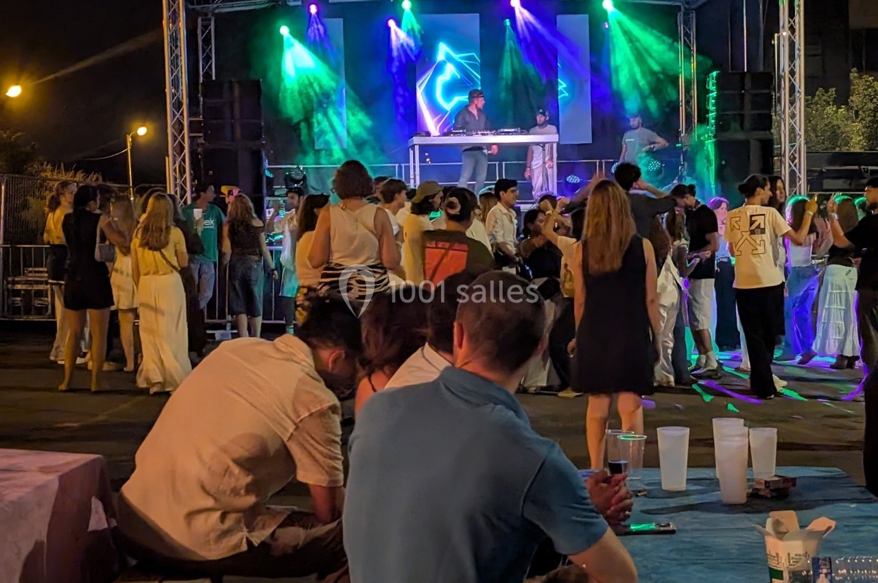 Groupe de personnes dansant et socialisant devant une scène illuminée avec un DJ lors d'un événement en soirée.