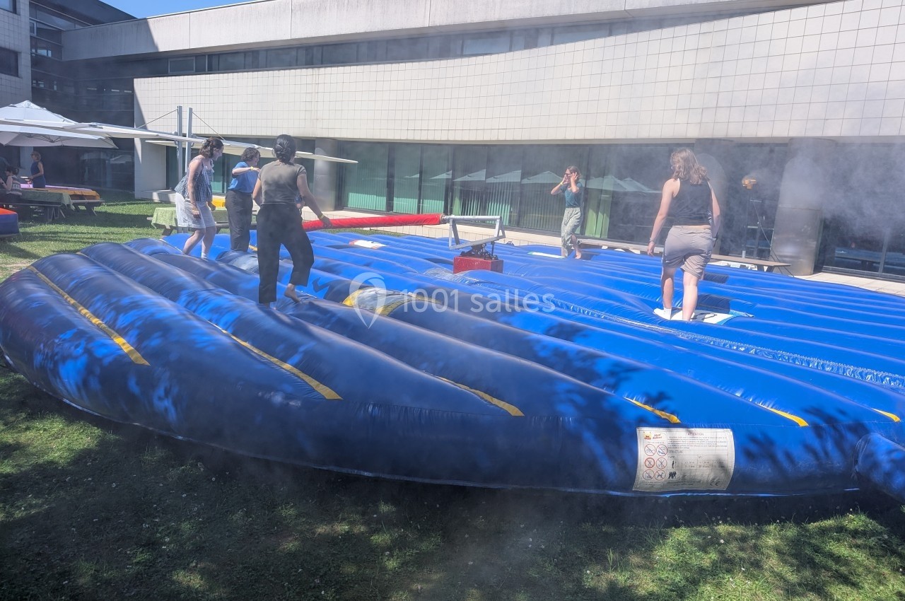 Des personnes marchent sur une structure gonflable bleue en extérieur, devant un bâtiment moderne.