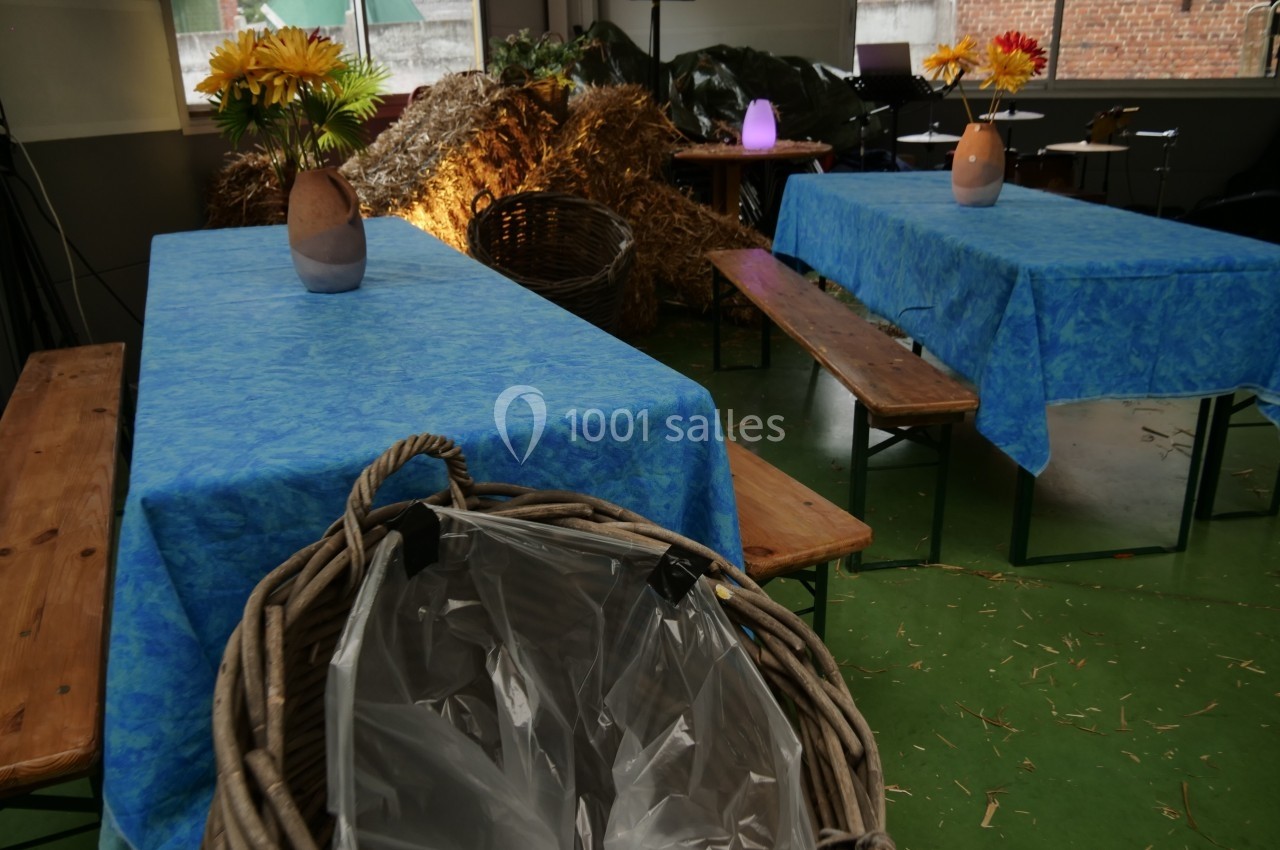 Tables recouvertes de nappes bleues avec des vases de fleurs, entourées de bancs en bois dans un décor rustique.
