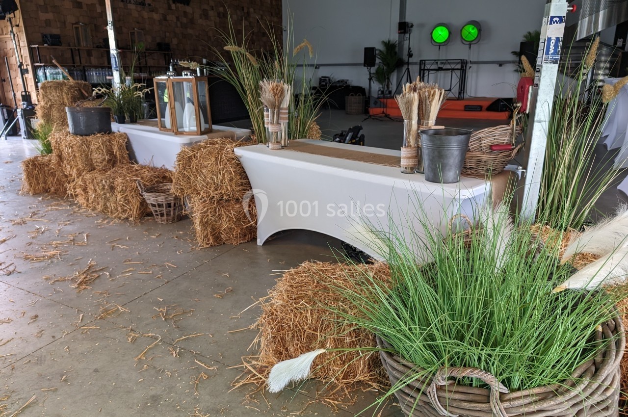 Décoration rustique avec bottes de paille, paniers d'herbes et tables recouvertes de nappes blanches dans un espace couvert.