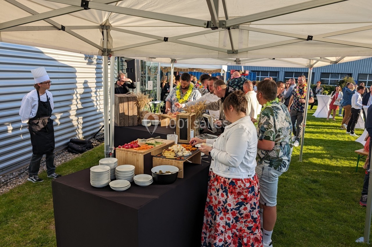Des personnes se servent à un buffet en plein air sous des tentes blanches, avec un chef en arrière-plan.