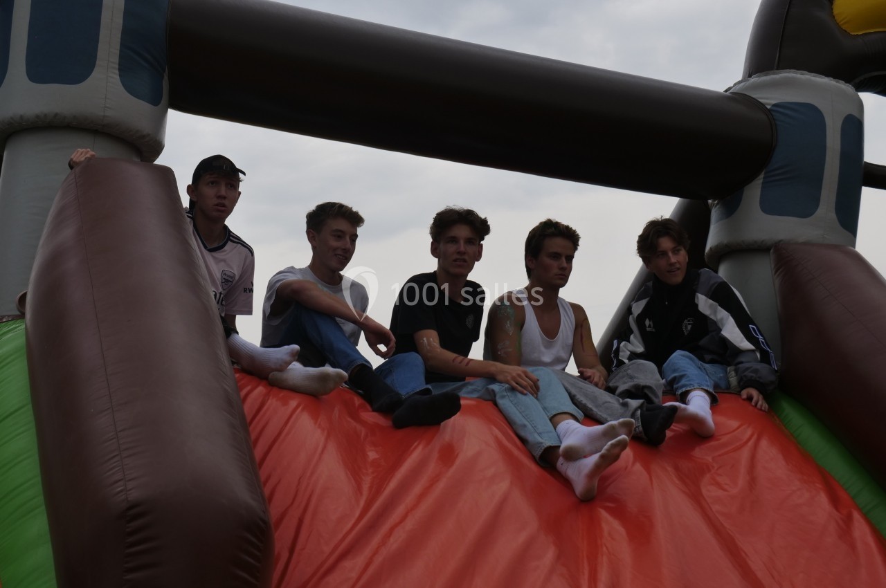 Cinq jeunes assis en haut d'un toboggan gonflable coloré sous un ciel nuageux.