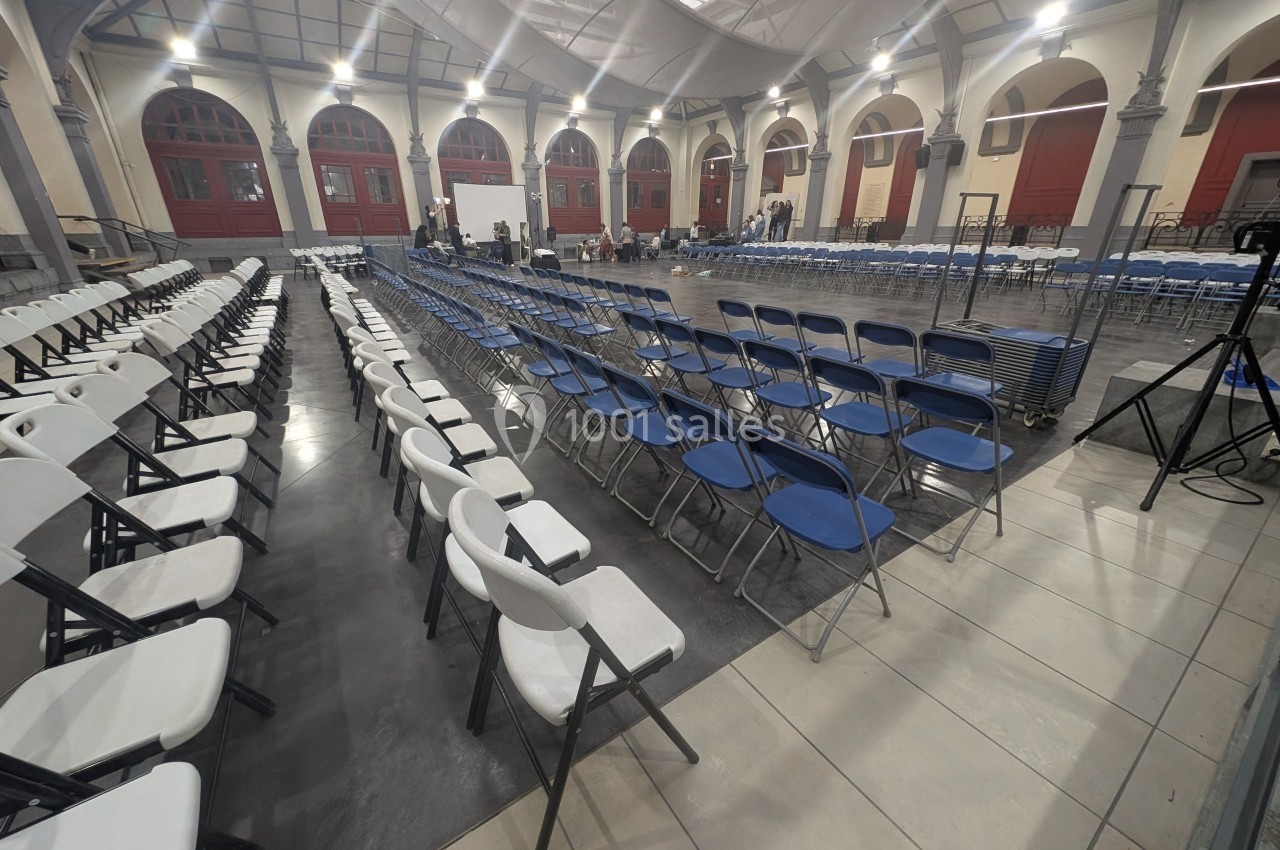 Salle avec des rangées de chaises blanches et bleues alignées, prête pour un événement ou une conférence.