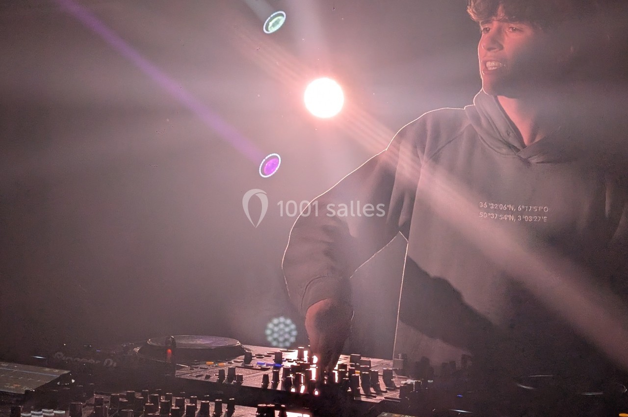 Un DJ mixe sur une table de mixage sous des lumières de scène tamisées.