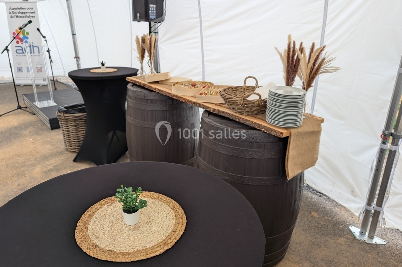 Deux tonneaux formant une table avec des assiettes, des paniers et des décorations, sous une tente blanche.