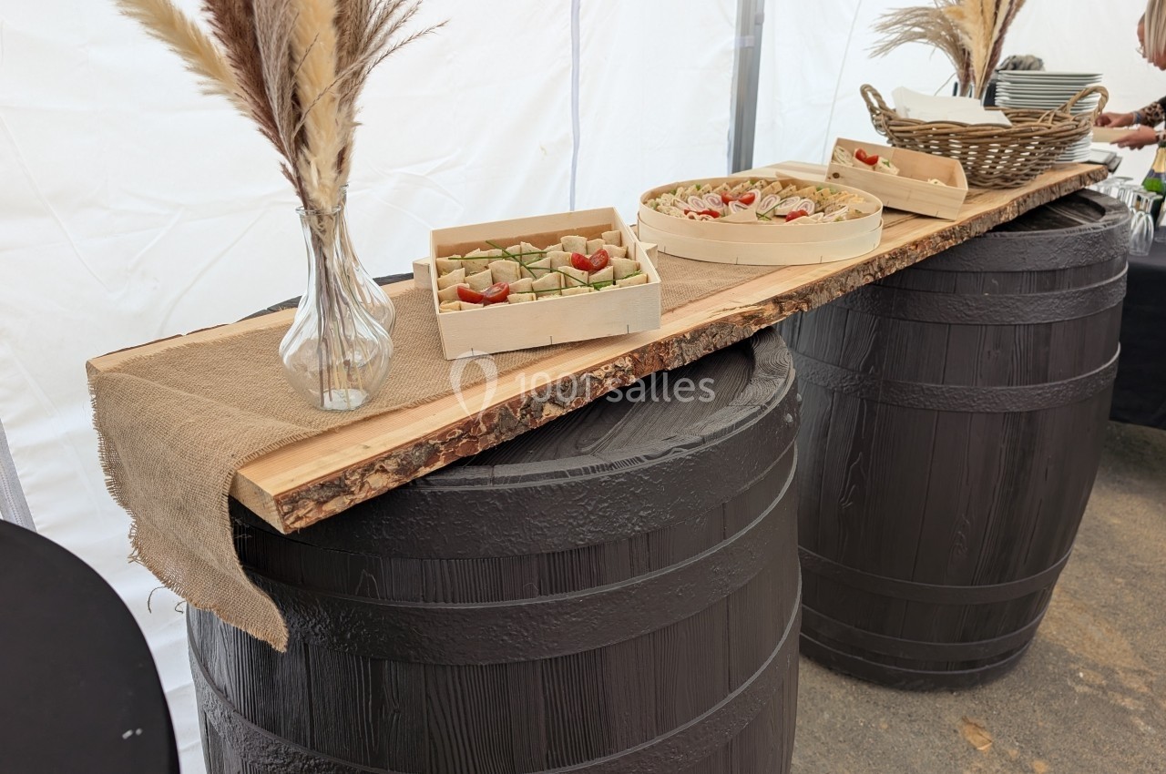 Buffet rustique avec plateaux de nourriture sur une planche en bois posée sur deux tonneaux, décoré de vases avec des herbes…