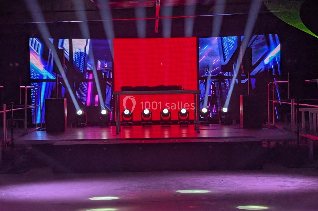 Scène avec éclairage coloré, écran rouge central, projecteurs et équipements audio dans un espace intérieur sombre.