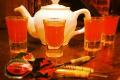 Terrasse de café avec des chaises en osier, tables vides et parasols, située dans une rue pavée bordée de bâtiments.