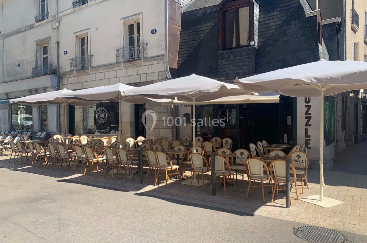 Terrasse d'un café-restaurant avec chaises en rotin et parasols, située dans une rue piétonne ensoleillée.