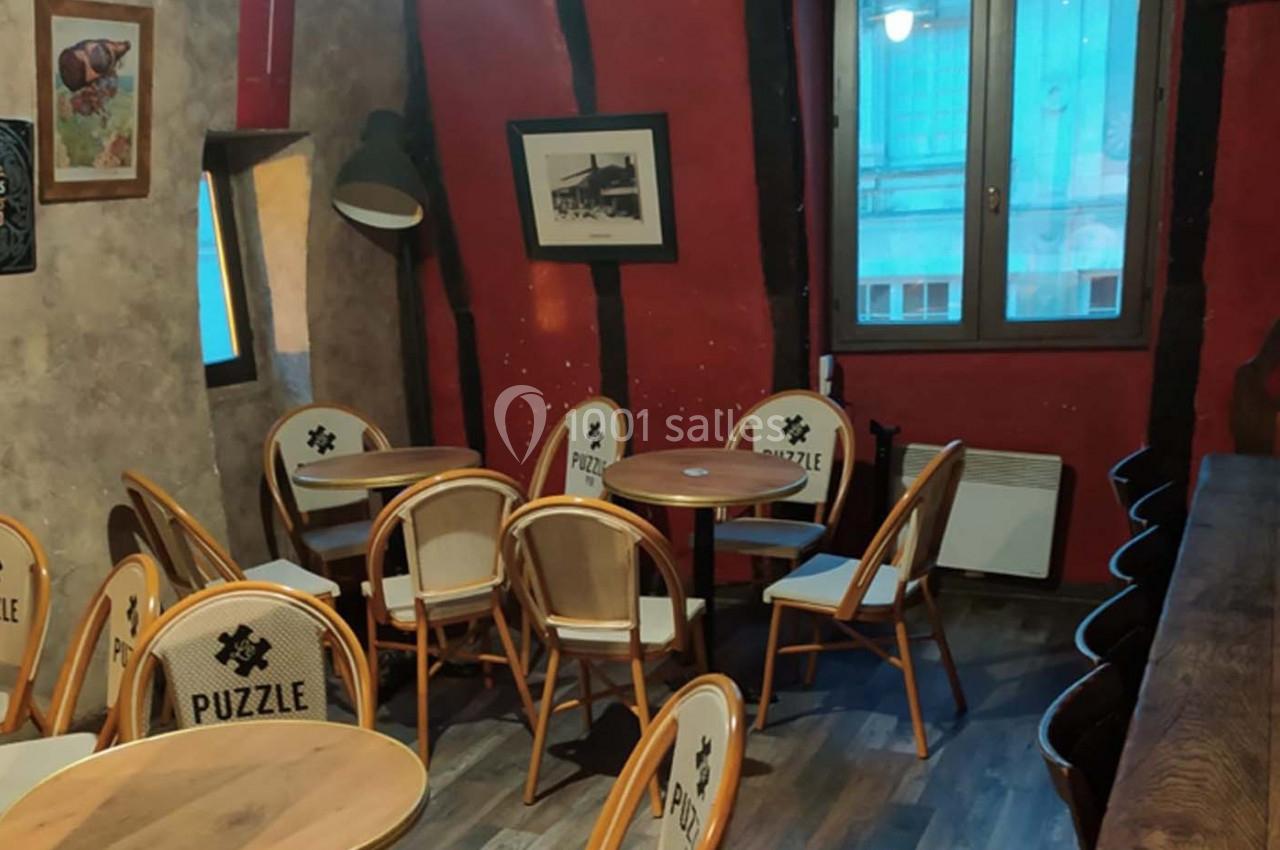 Salle de café avec des tables rondes, des chaises en bois clair et un mur rouge décoré de cadres.