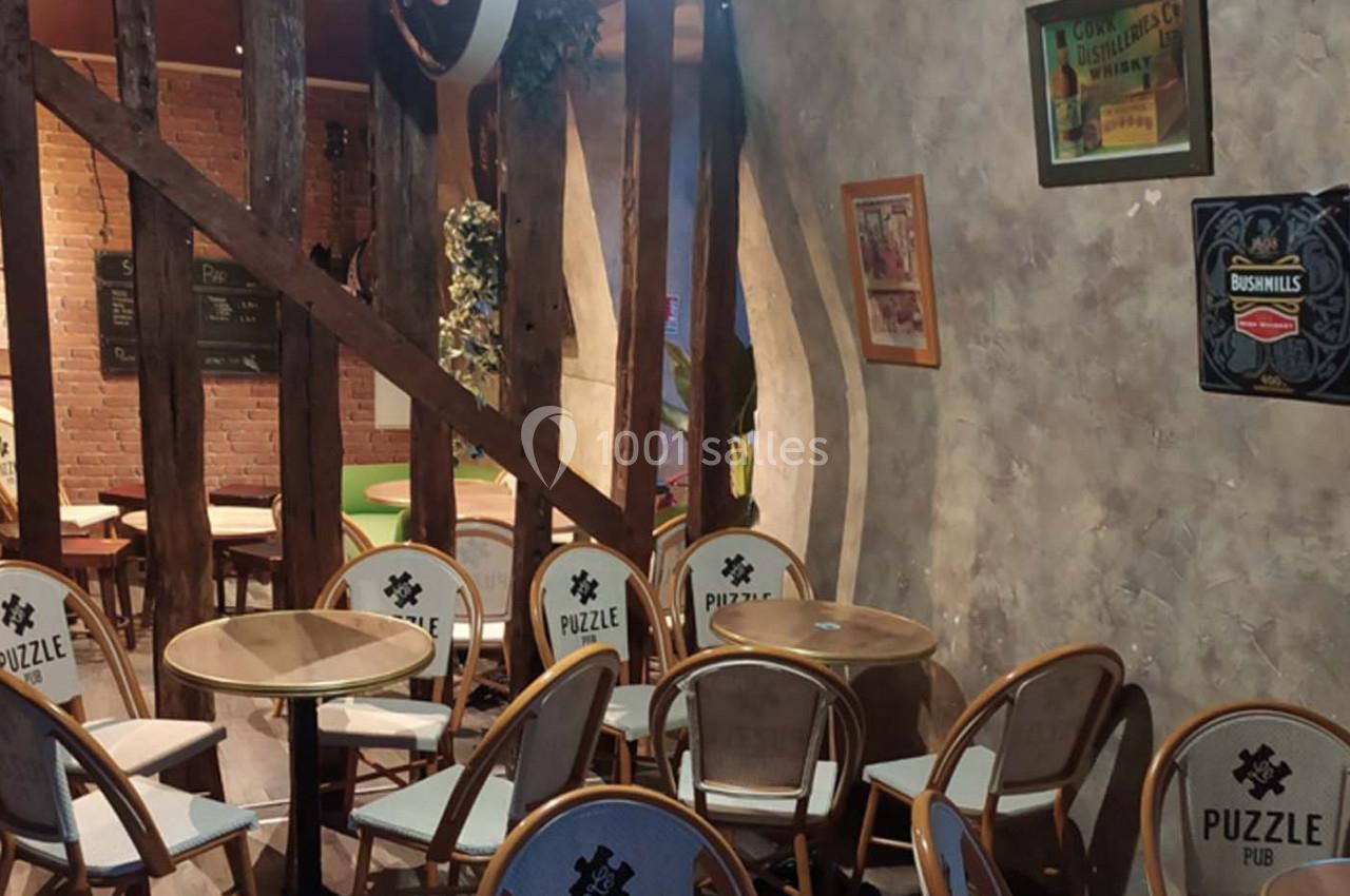 Salle d'un pub avec des chaises et tables en bois, murs en pierre et affiches décoratives accrochées.