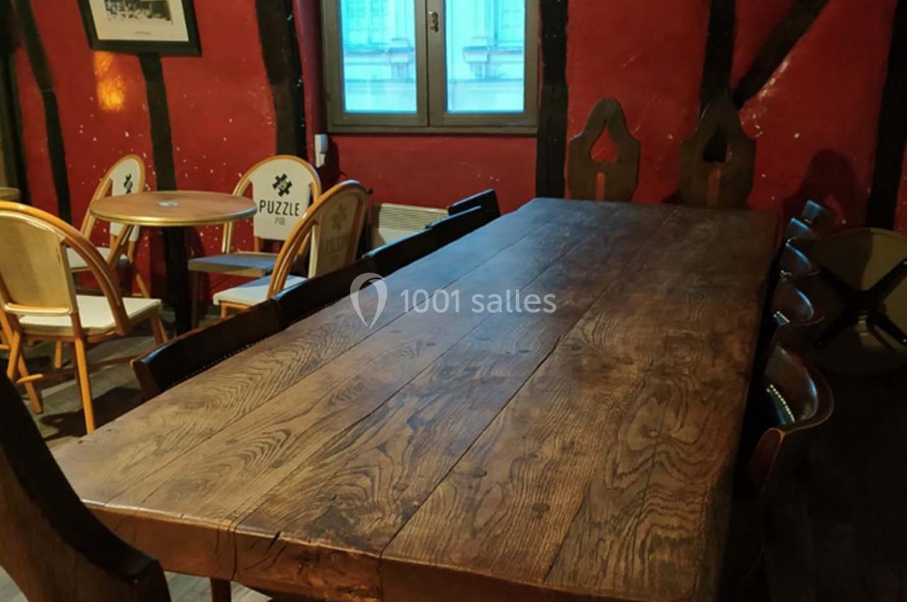 Grande table en bois rustique entourée de chaises dans une pièce aux murs rouges avec poutres apparentes.