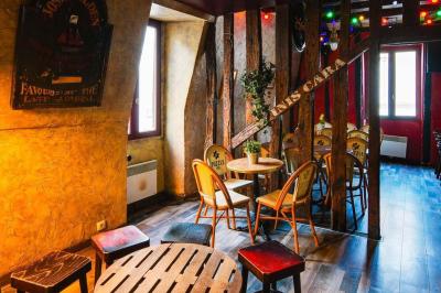 Terrasse de café avec des chaises en osier, tables vides et parasols, située dans une rue pavée bordée de bâtiments.