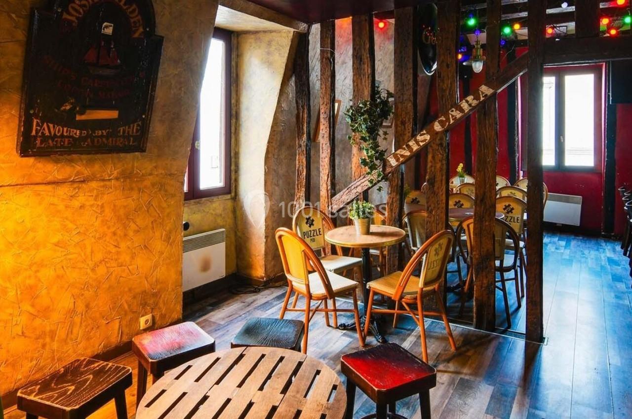 Salle chaleureuse avec murs texturés, mobilier en bois, éclairage coloré et grandes fenêtres laissant entrer la lumière.