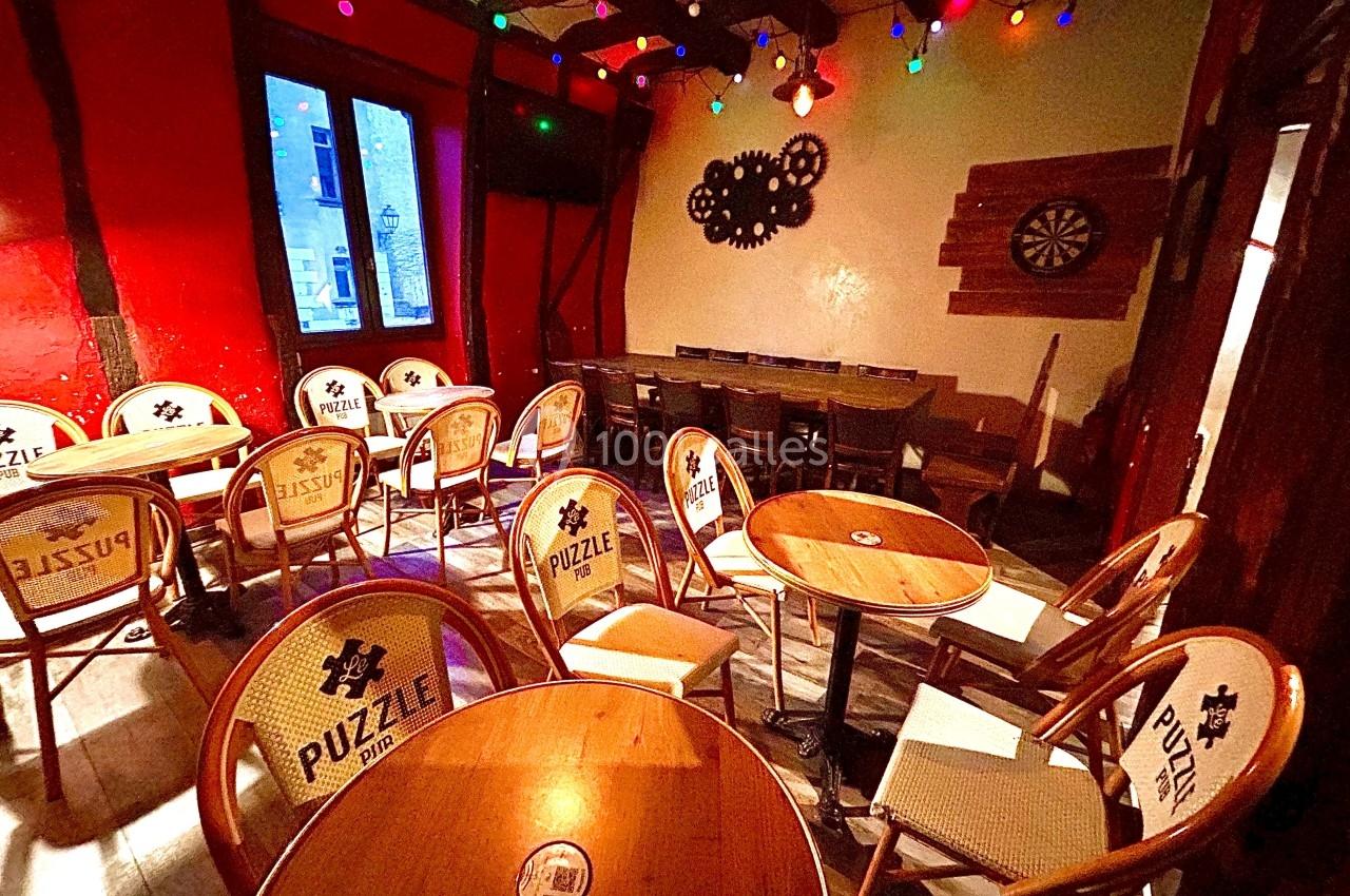 Salle de café avec des tables rondes en bois, chaises en rotin et guirlandes lumineuses colorées au plafond.