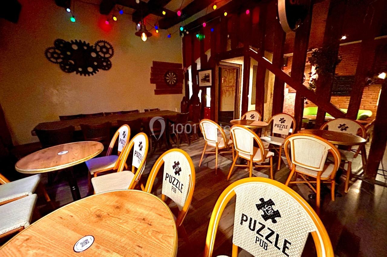 Salle de bar avec tables en bois, chaises personnalisées ’Puzzle Pub’, éclairage chaleureux et guirlandes lumineuses…