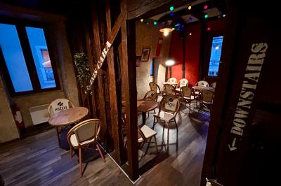 Terrasse de café avec des chaises en osier, tables vides et parasols, située dans une rue pavée bordée de bâtiments.