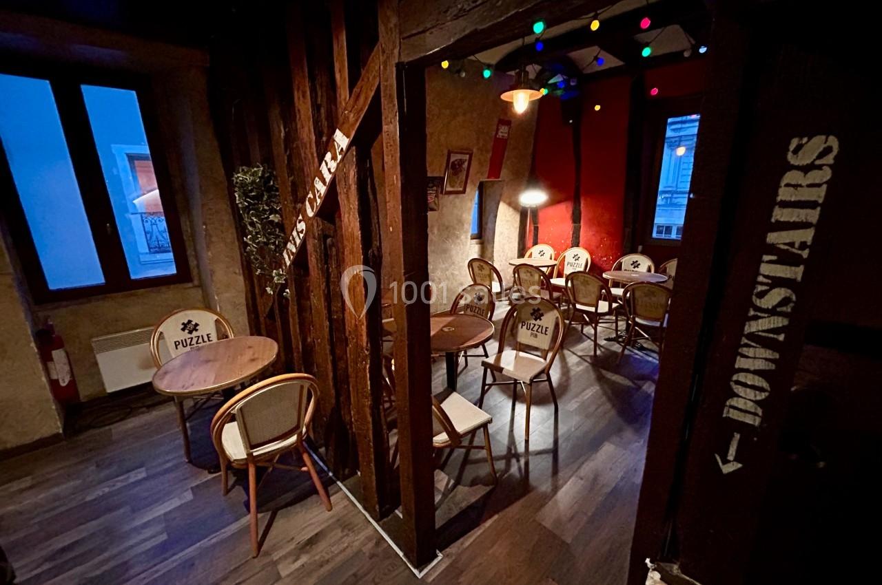 Salle intérieure chaleureuse avec tables, chaises en bois et guirlandes lumineuses colorées, ambiance conviviale.