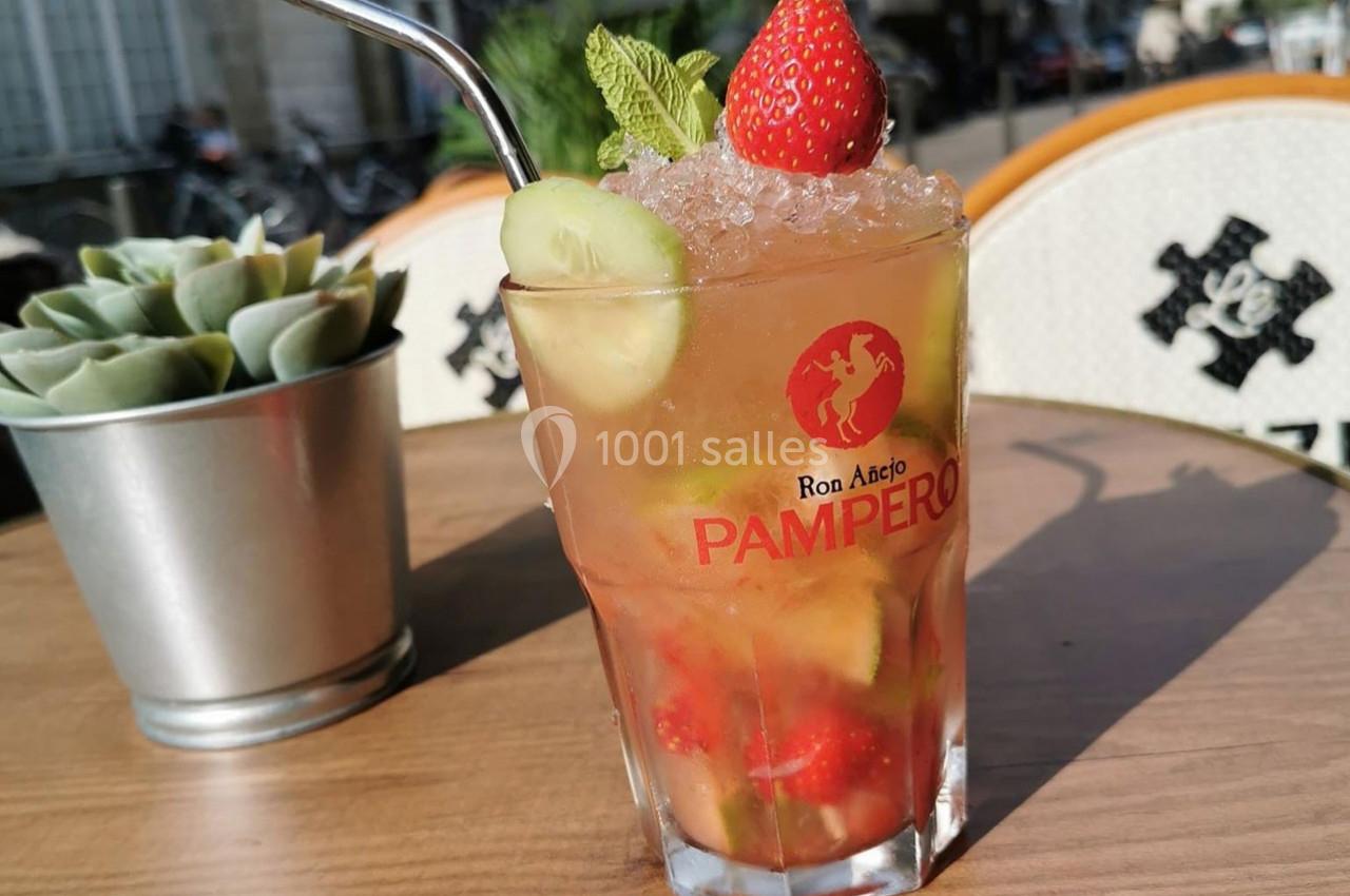 Verre de cocktail fruité avec fraise, concombre, menthe et glaçons, posé sur une table en terrasse ensoleillée.
