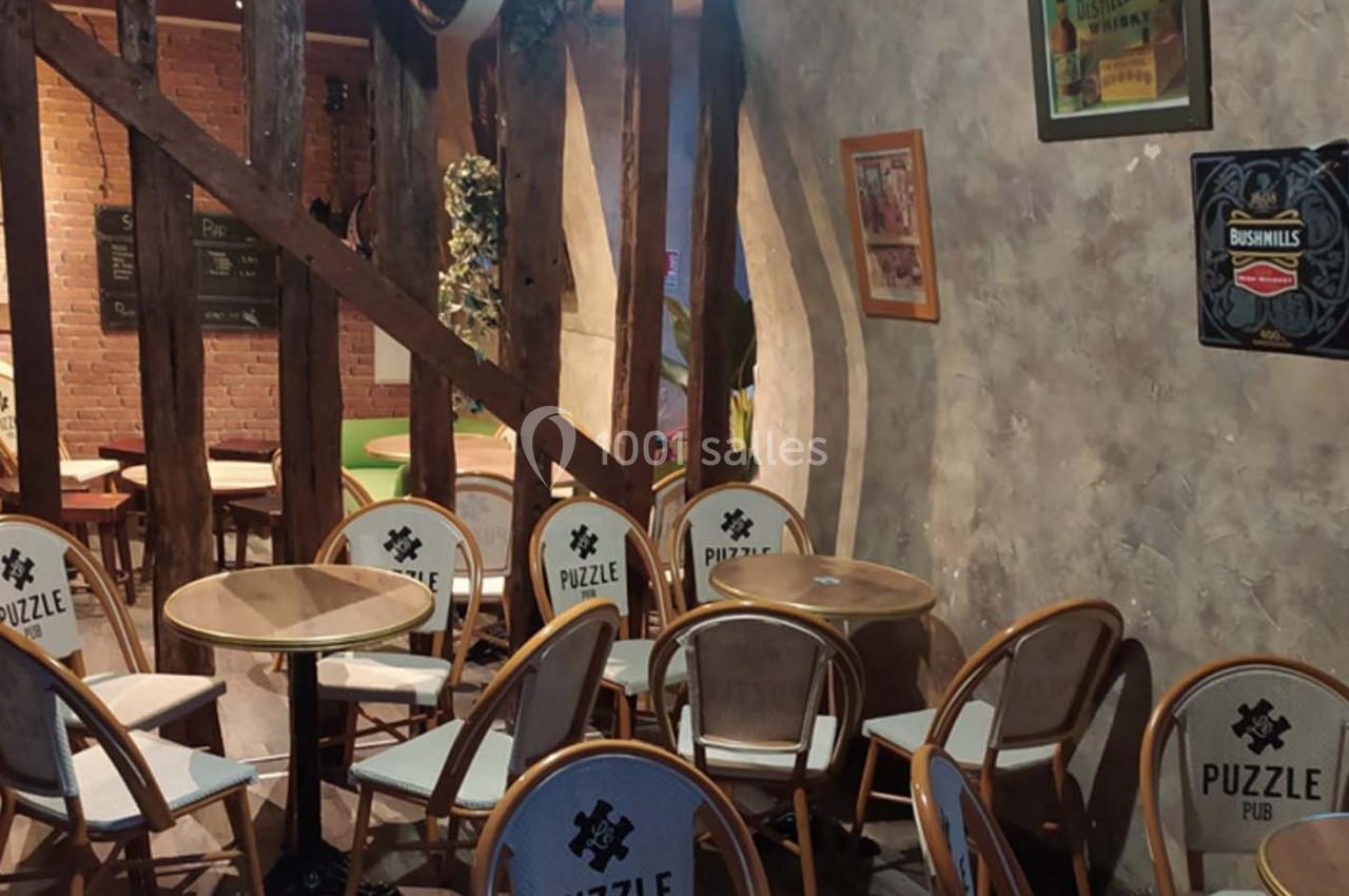 Chaises et tables en bois dans un espace intérieur avec murs texturés, poutres apparentes et décorations murales.