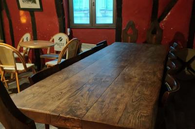 Grande table en bois massif entourée de chaises dans une pièce aux murs rouges avec poutres apparentes.