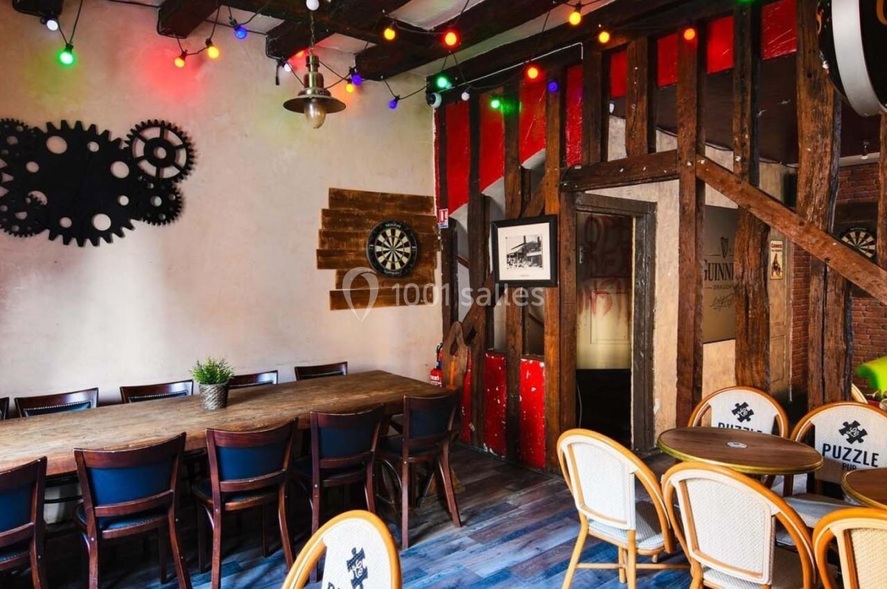 Salle conviviale avec grande table en bois, chaises, décorations murales colorées et guirlandes lumineuses.