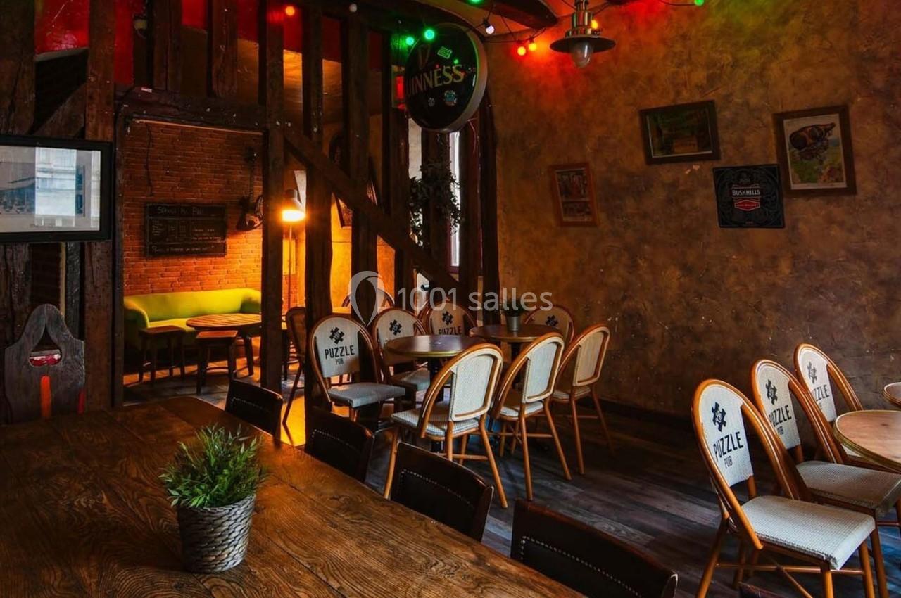 Salle chaleureuse avec murs en bois et briques, éclairage tamisé, tables en bois et chaises disposées autour.