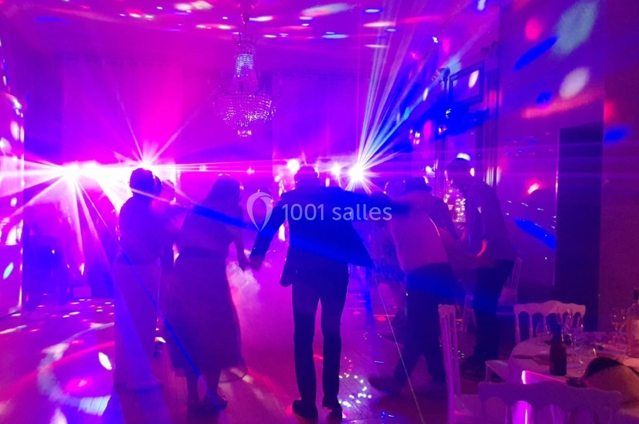 Des personnes dansent sous des lumières colorées dans une salle éclairée par un lustre.