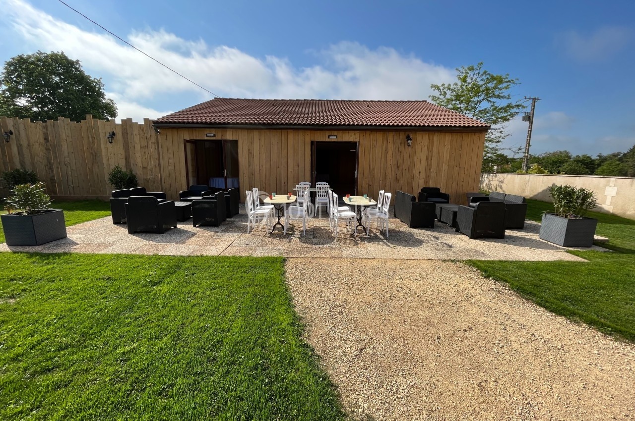 Espace extérieur avec mobilier de jardin devant un bâtiment en bois, entouré de pelouse et d'une clôture.
