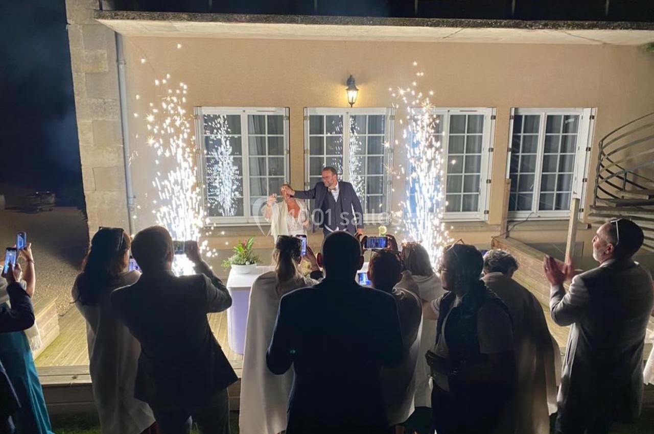 Un couple coupe un gâteau de mariage devant des invités, entouré de gerbes d'étincelles et de lumière.