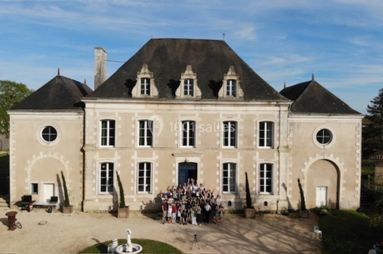 Façade d'un château ancien en pierre avec un groupe de personnes rassemblées devant l'entrée principale.
