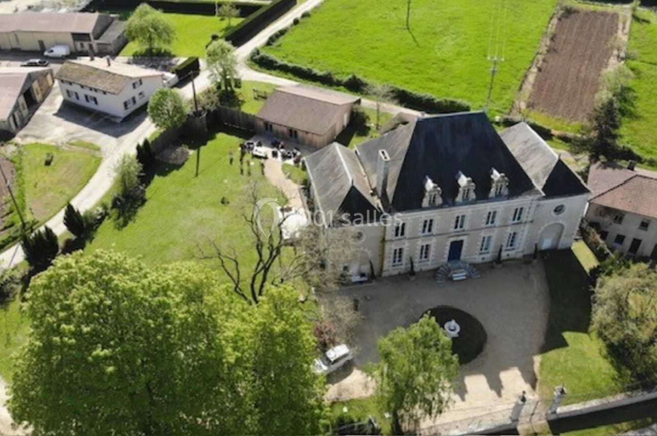 Vue aérienne d'un manoir entouré de jardins, avec des bâtiments annexes et des champs à proximité.
