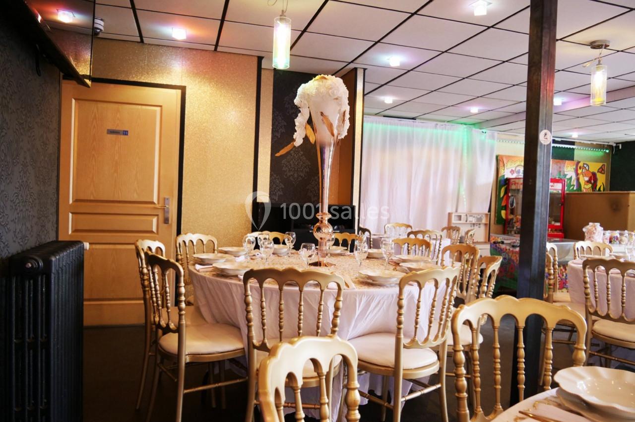 Salle de réception décorée avec des tables rondes, chaises dorées et un centre de table floral élégant.