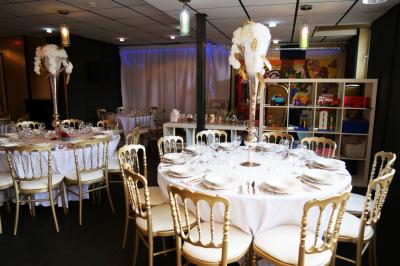 Terrasse en bois avec fauteuils, pergola à rideaux blancs, plantes en pot et mur en briques en arrière-plan.