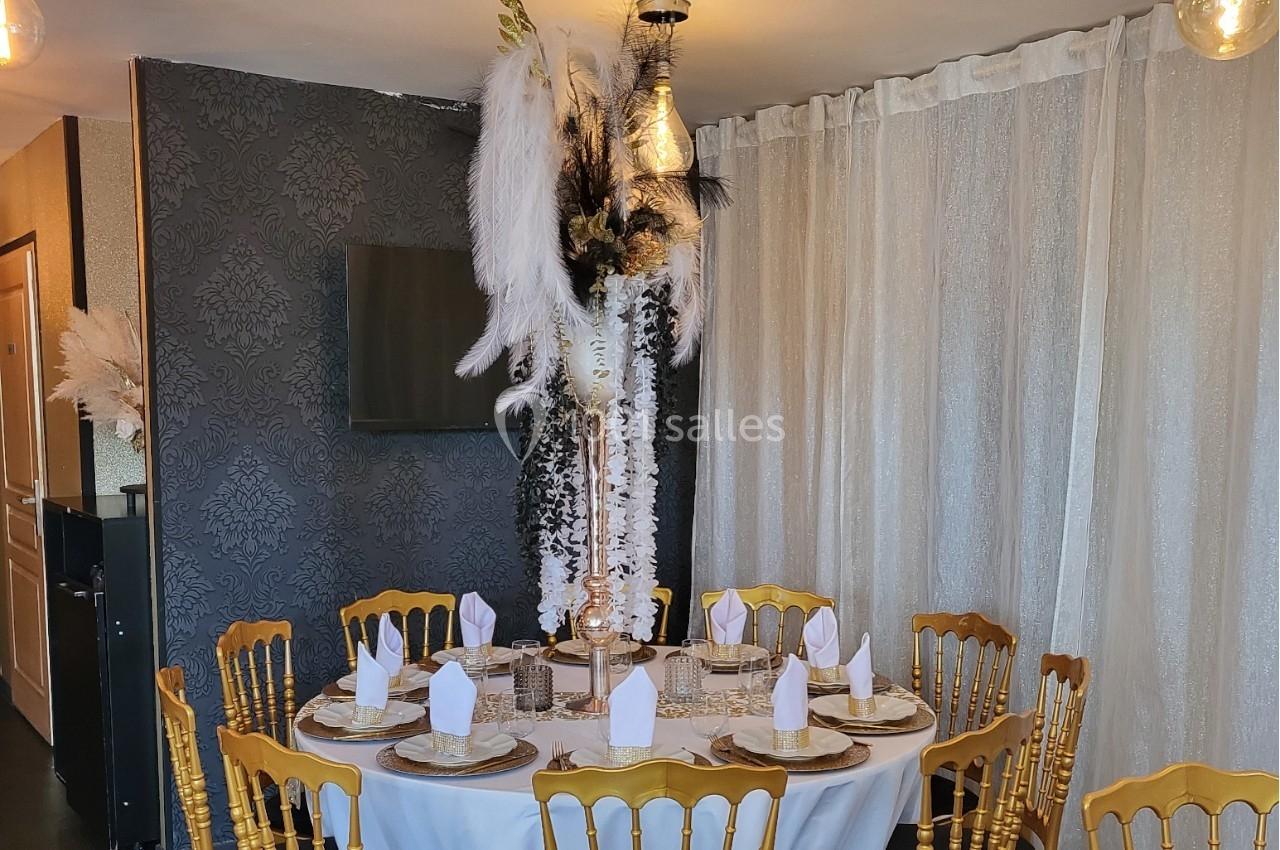 Table ronde élégamment dressée avec des chaises dorées, décorée de plumes blanches et noires dans une salle raffinée.