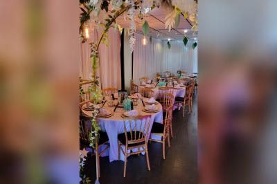 Terrasse en bois avec fauteuils, pergola à rideaux blancs, plantes en pot et mur en briques en arrière-plan.