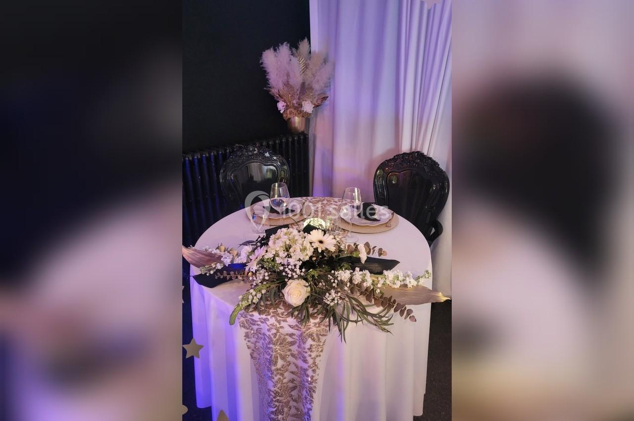 Table ronde élégamment dressée pour deux, avec décoration florale blanche et pampas en arrière-plan.