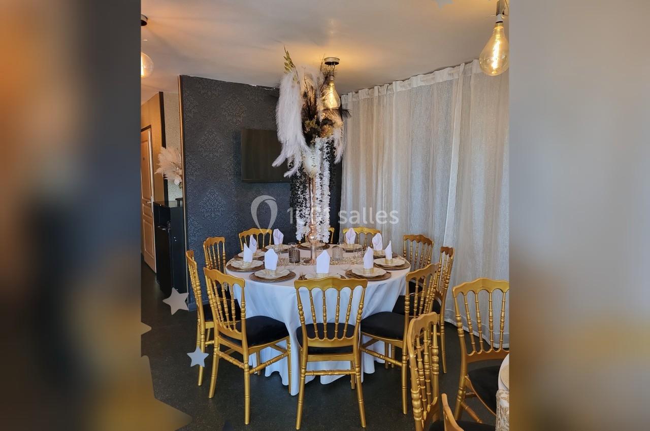 Table ronde décorée pour un événement, entourée de chaises dorées, avec un centre de table orné de plumes blanches.