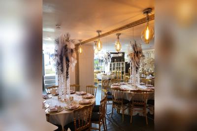 Terrasse en bois avec fauteuils, pergola à rideaux blancs, plantes en pot et mur en briques en arrière-plan.