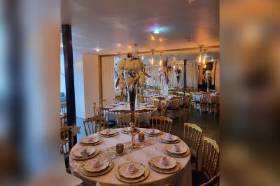 Terrasse en bois avec fauteuils, pergola à rideaux blancs, plantes en pot et mur en briques en arrière-plan.