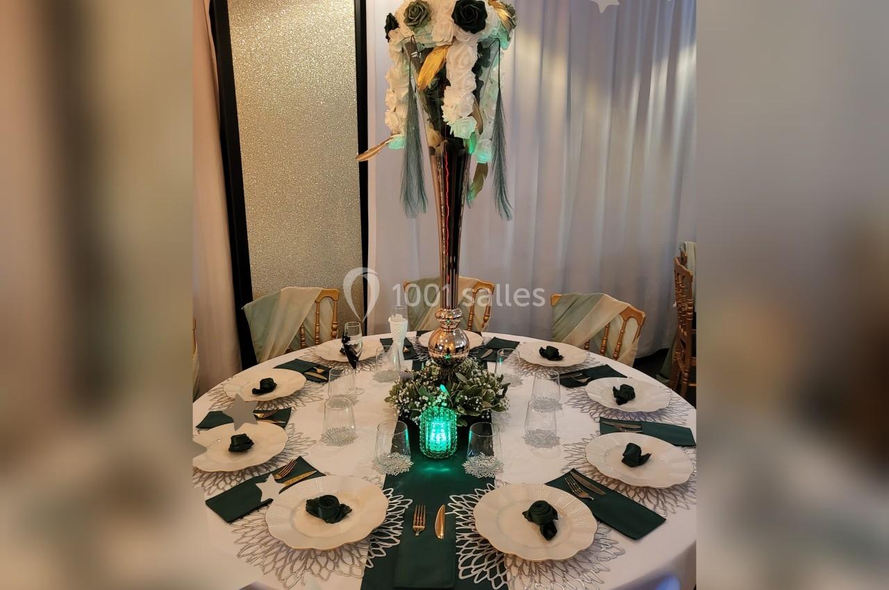 Table ronde élégamment dressée avec des assiettes blanches, serviettes vertes et un centre de table floral surélevé.