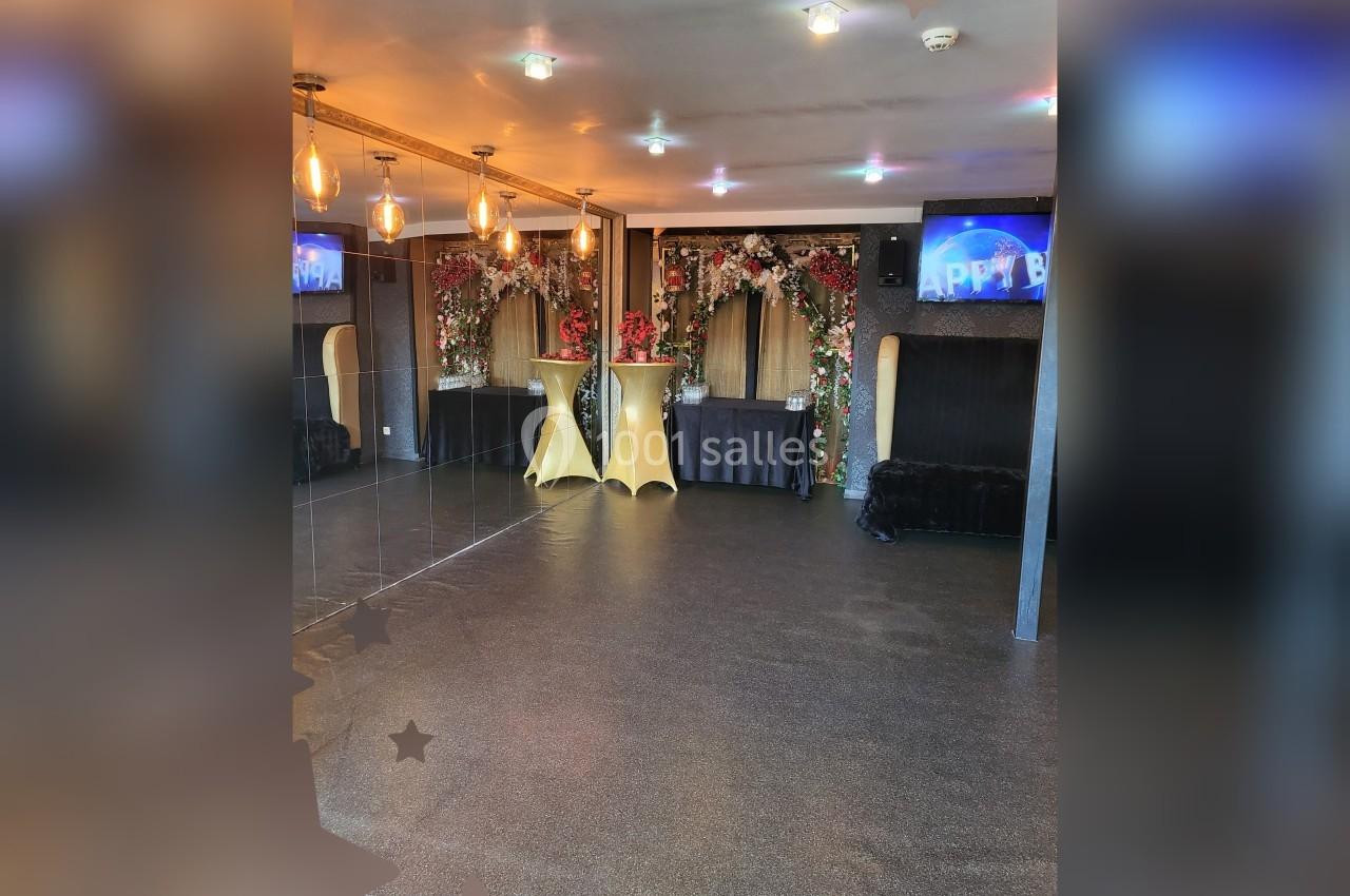 Salle décorée avec des arches fleuries, des tables hautes dorées et des écrans affichant ’Happy Birthday’.