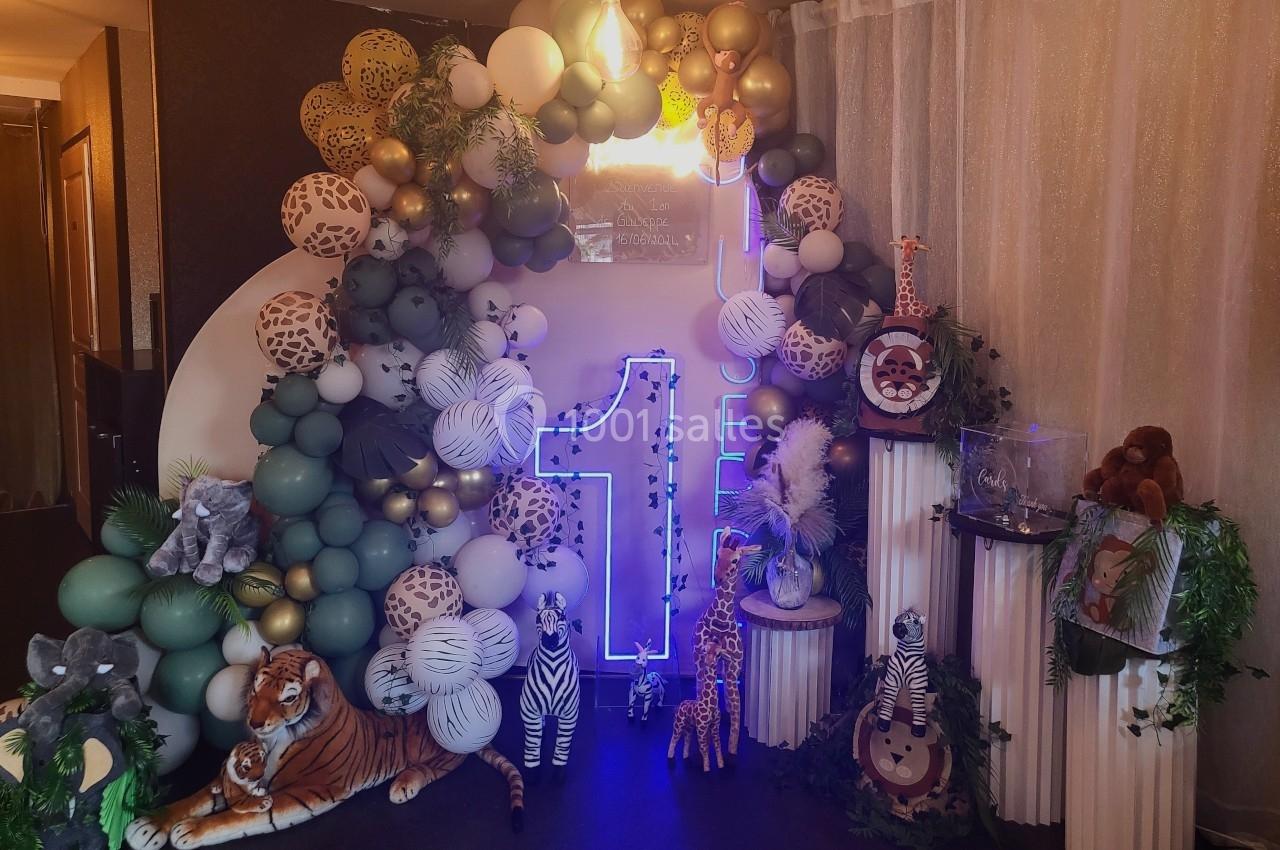 Décoration festive avec ballons, animaux en peluche et un chiffre ’1’ lumineux, dans un thème jungle.