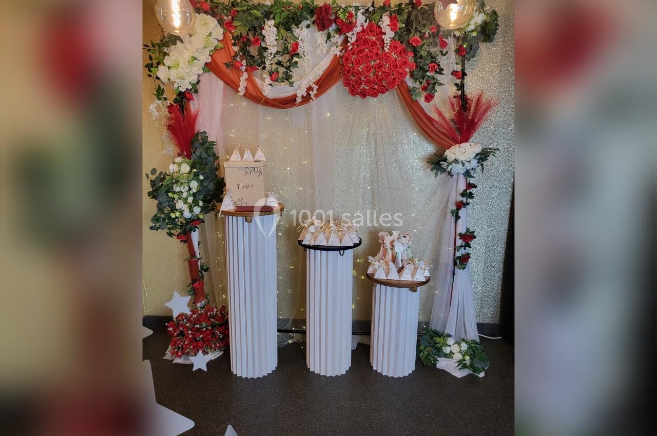 Décoration de fête avec arche florale rouge et blanche, colonnes blanches portant des boîtes cadeaux.
