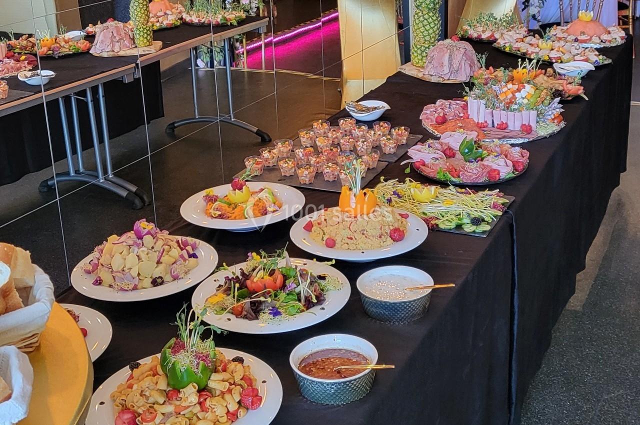 Buffet varié avec plats colorés, salades, verrines et sauces disposés sur des tables noires dans un cadre intérieur.