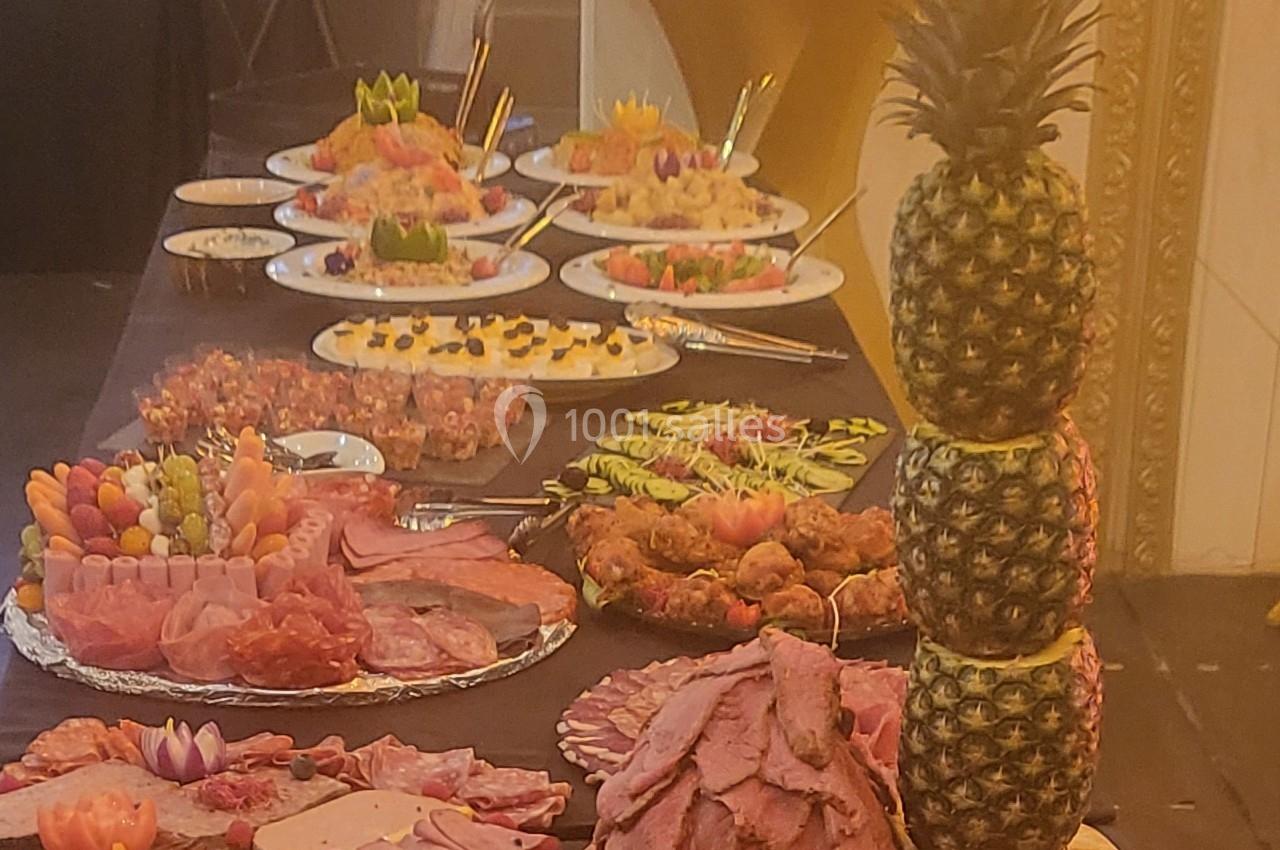 Buffet avec plats variés, incluant charcuterie, fruits, desserts et une décoration d'ananas empilés.