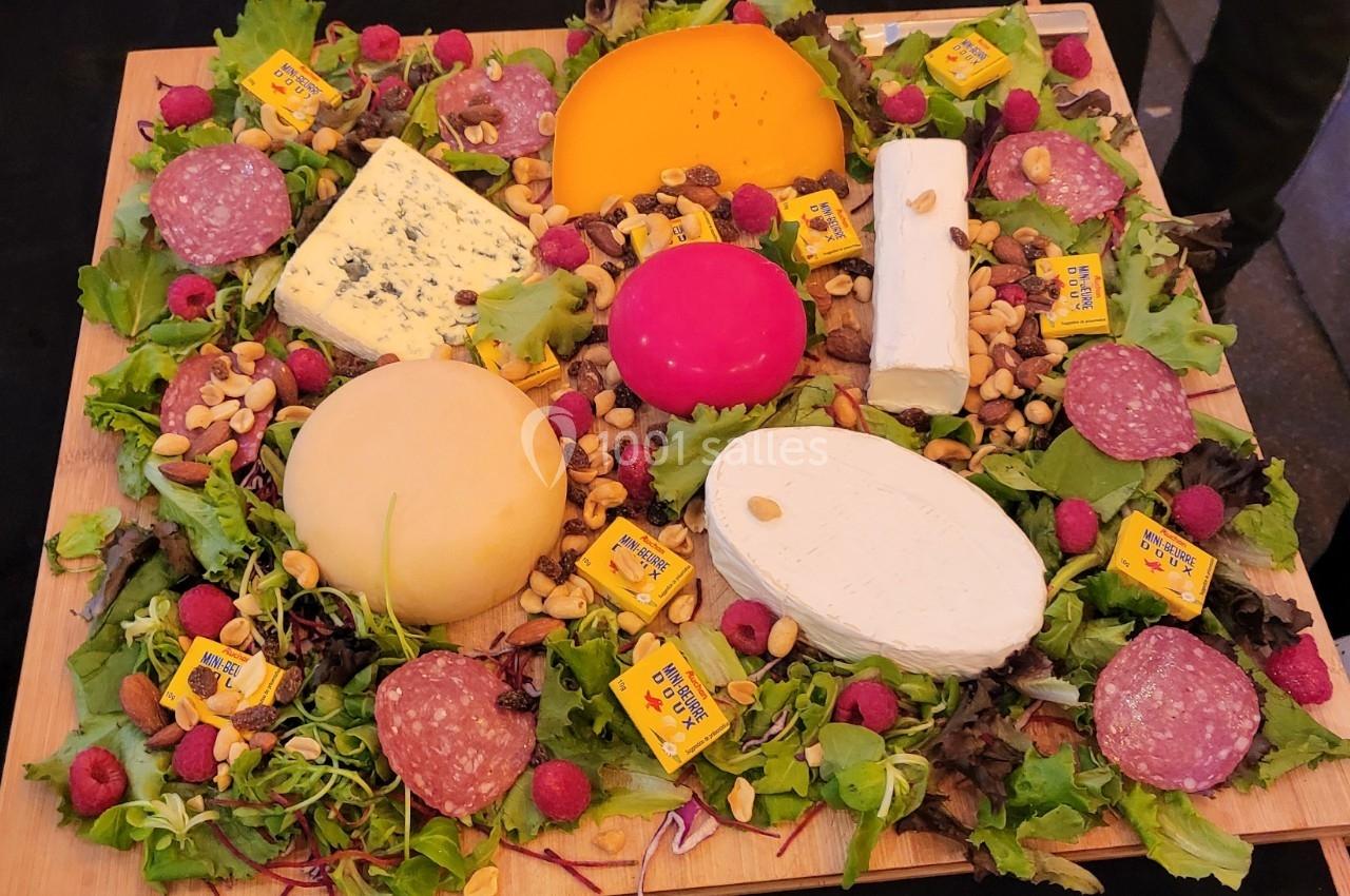 Plateau garni de fromages variés, charcuterie, framboises, noix et salade sur une planche en bois.